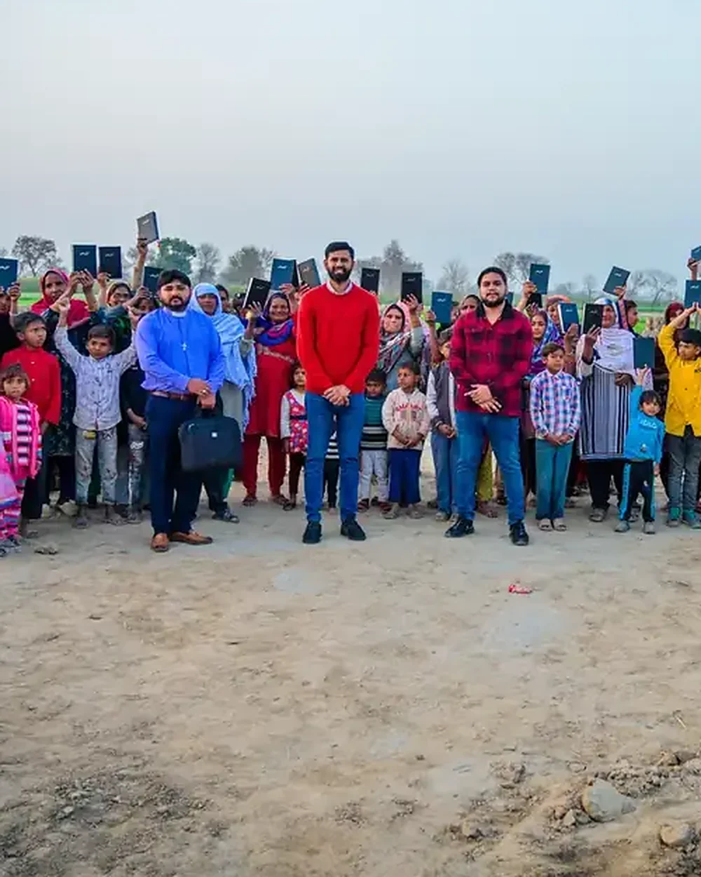 A whole village at the brick kilns holding up the Bibles they have just received