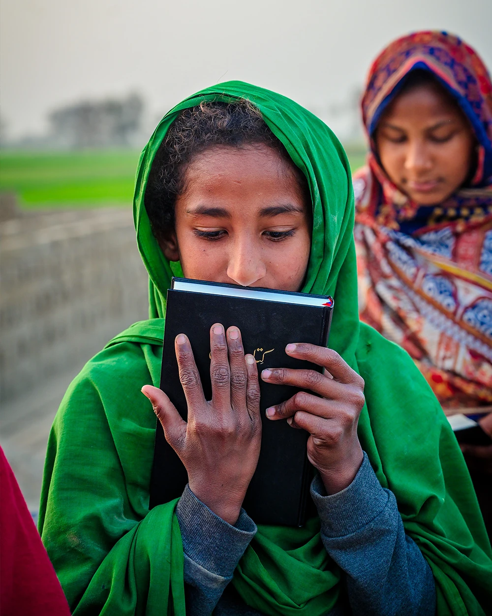 A girl at the brick kilns holding to her face the Bible she has just been given