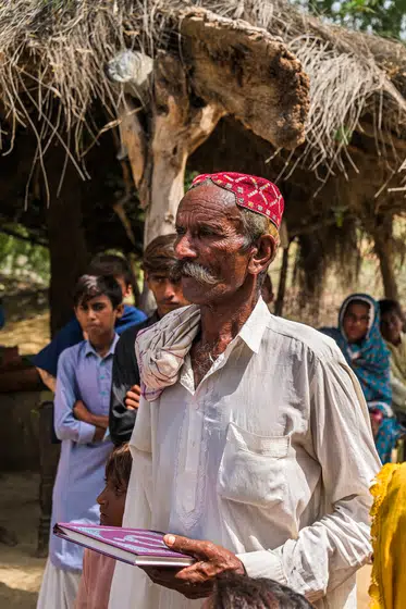 An elder holds an open Bible outside his home